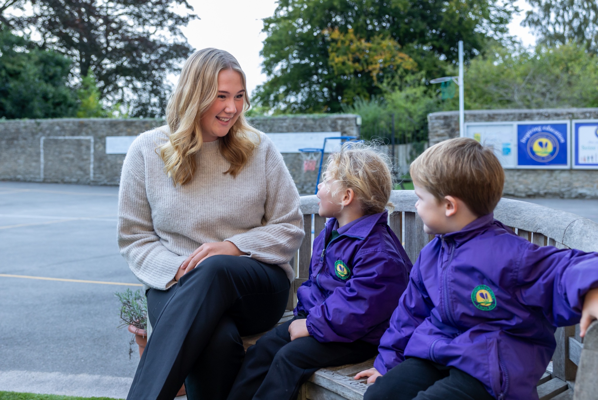 A staff member sits with two pupils on on a bench. They are smiling.